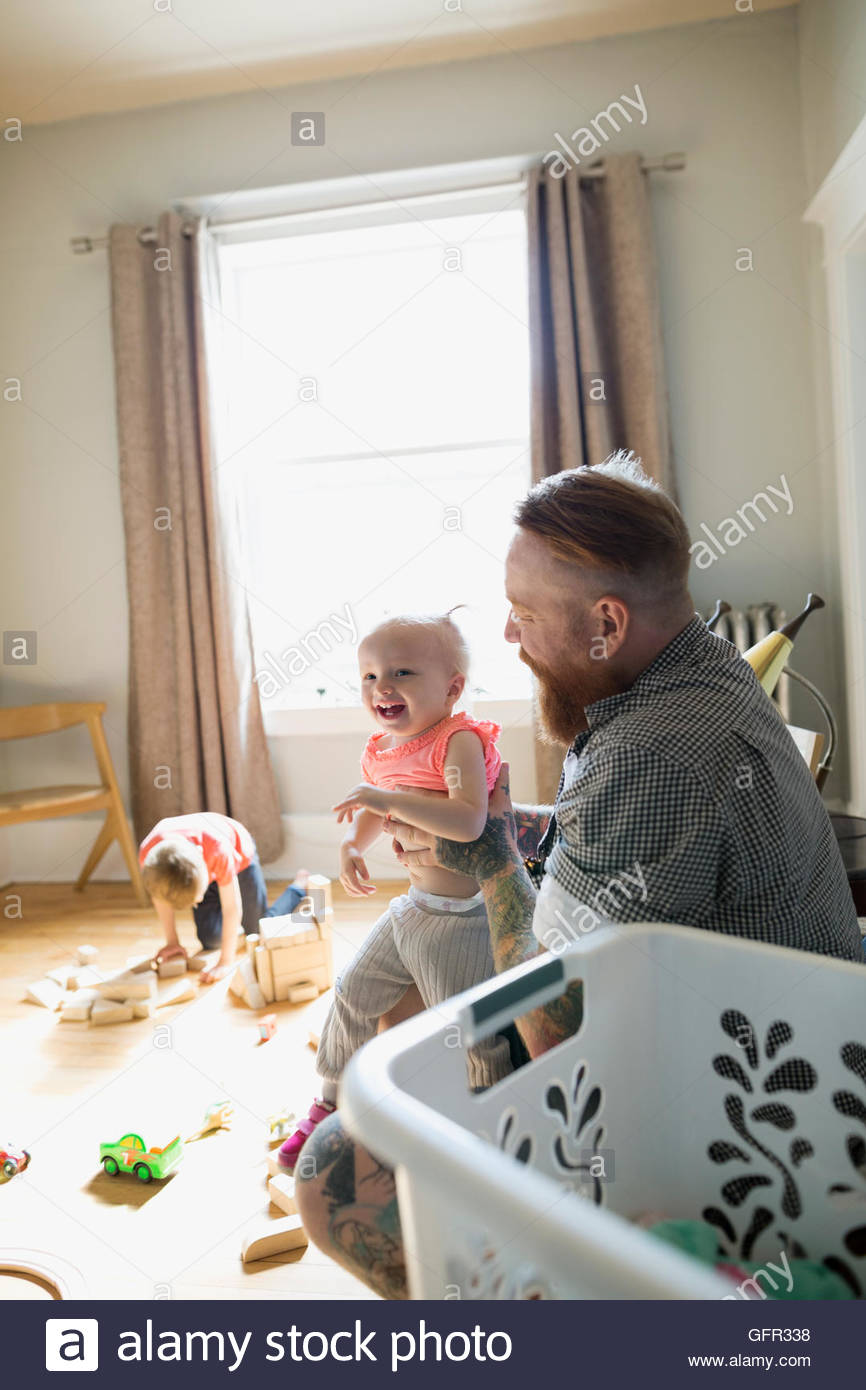 Father holding happy daughter on lap next to laundry basket Stock Photo