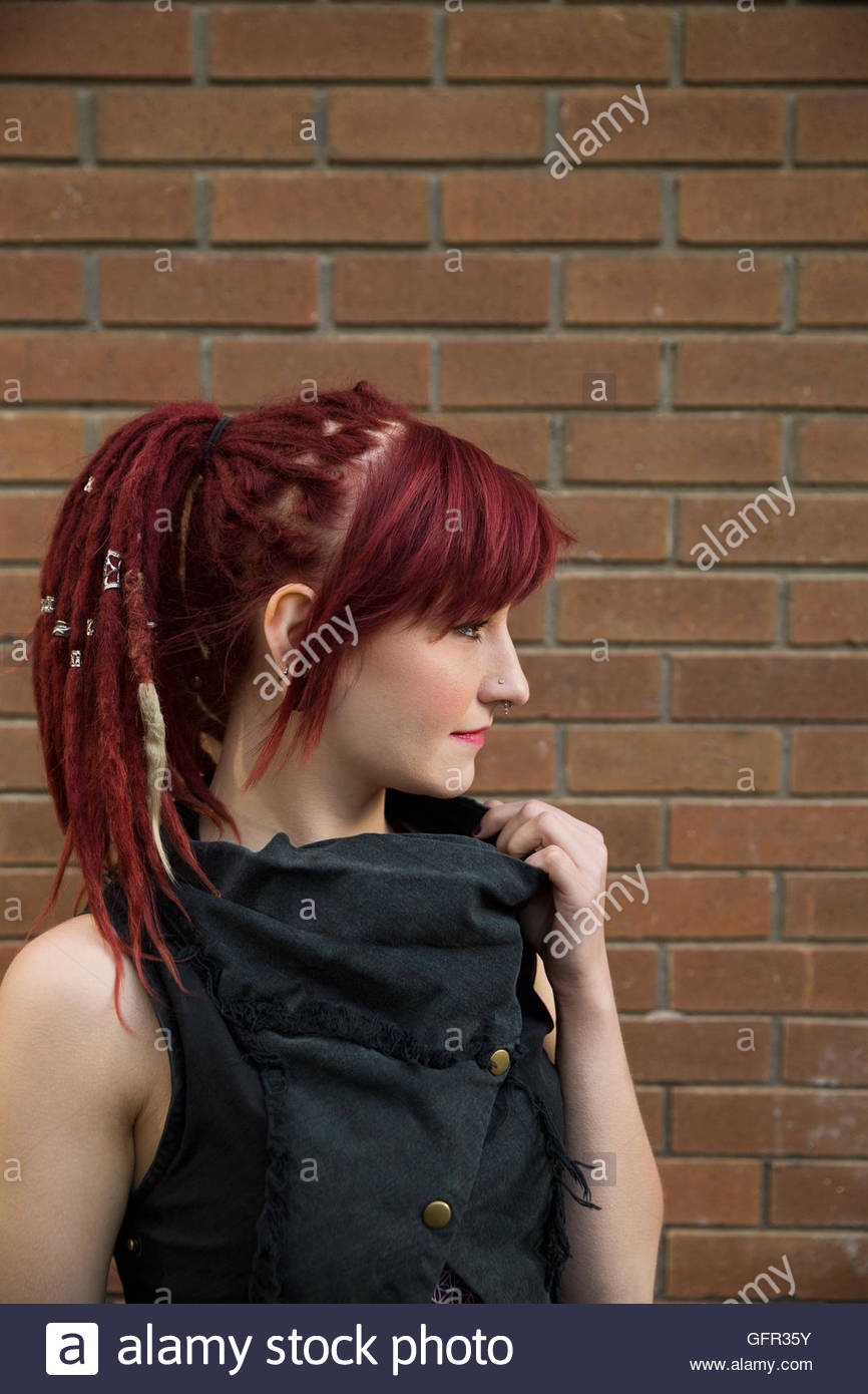 Cool woman with red dreadlocks looking away at brick wall Stock Photo