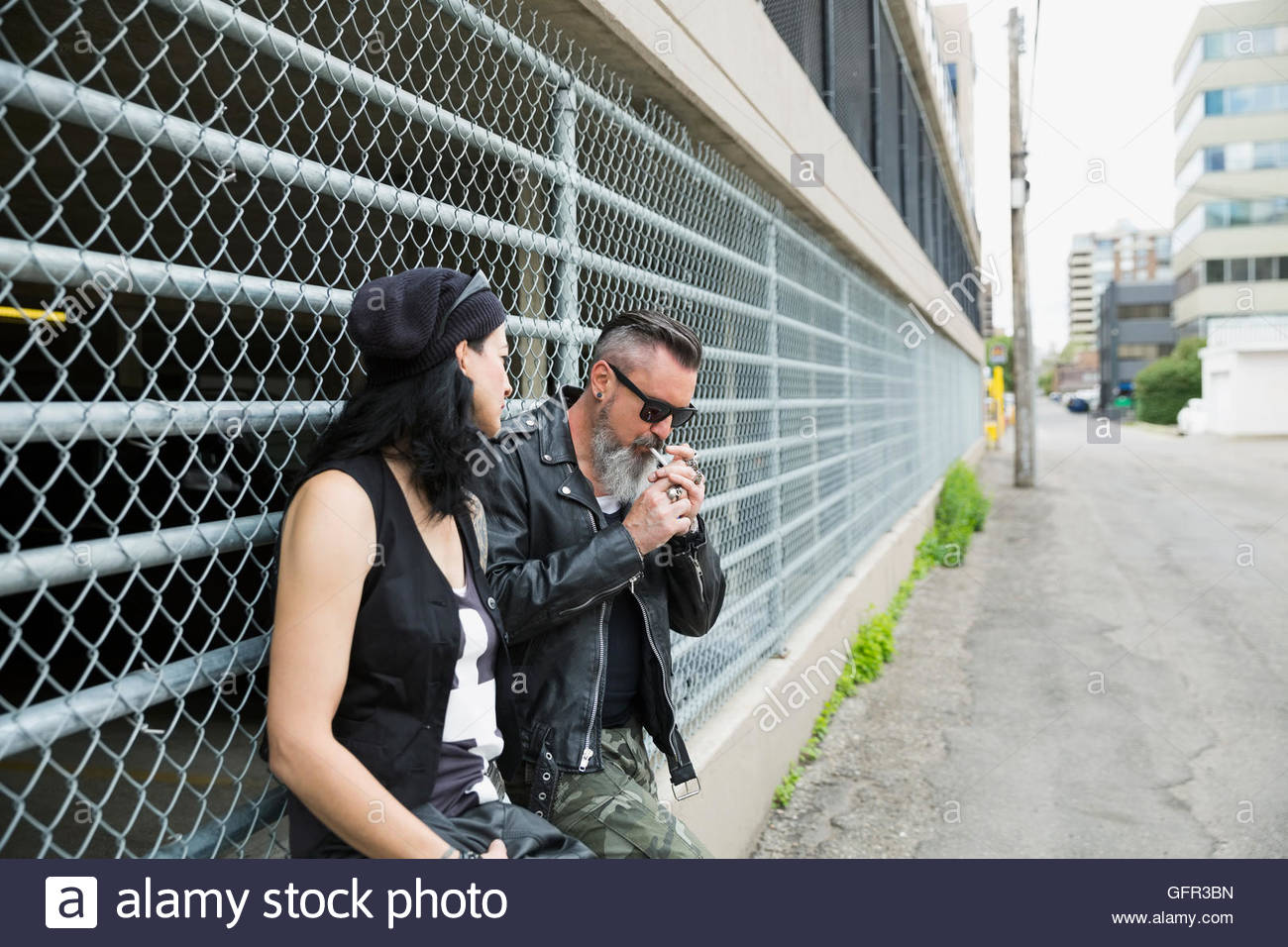 Cool mature couple smoking cigarette at urban fence Stock Photo