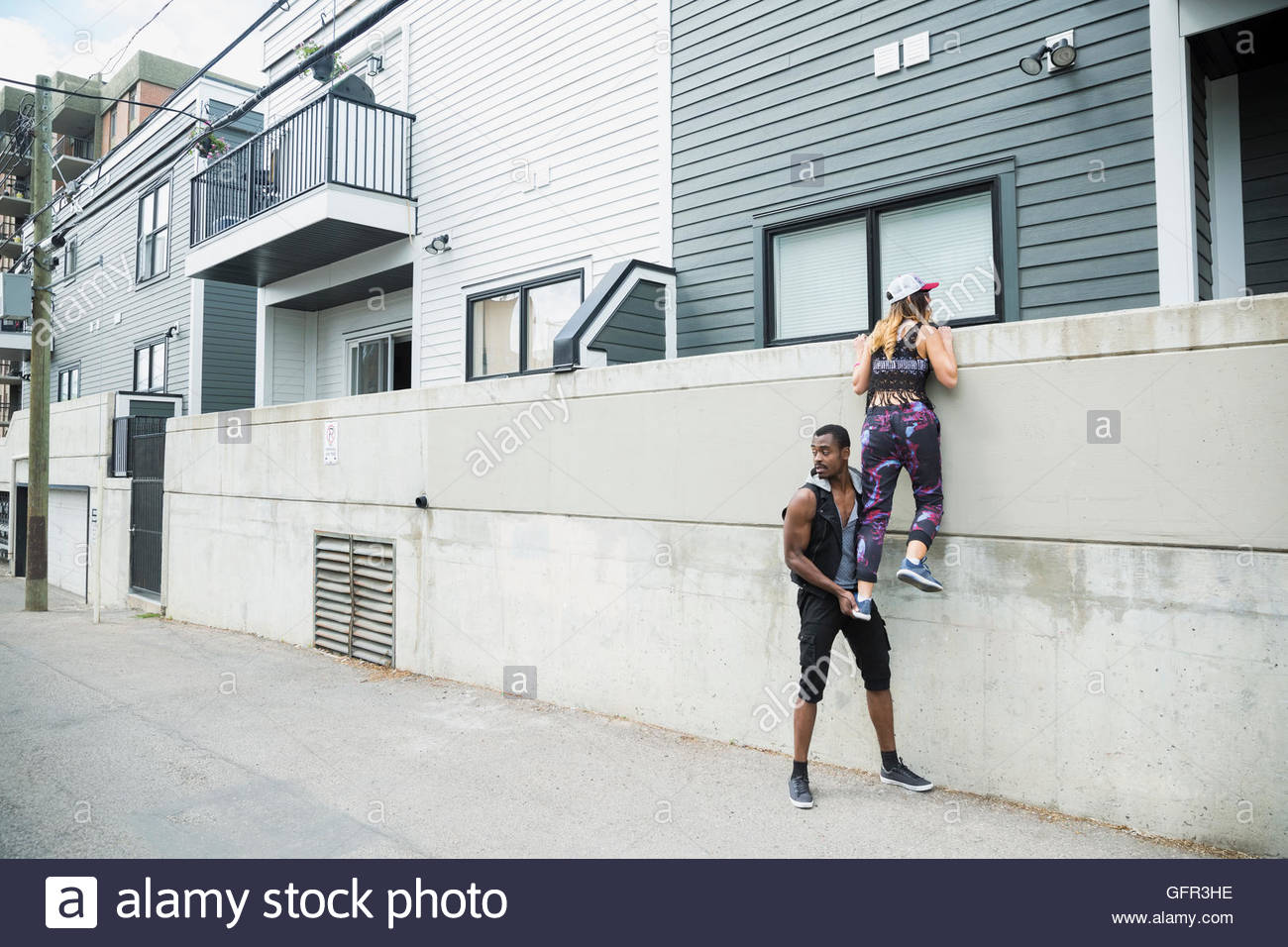 Suspicious young man lifting young woman over urban wall Stock Photo