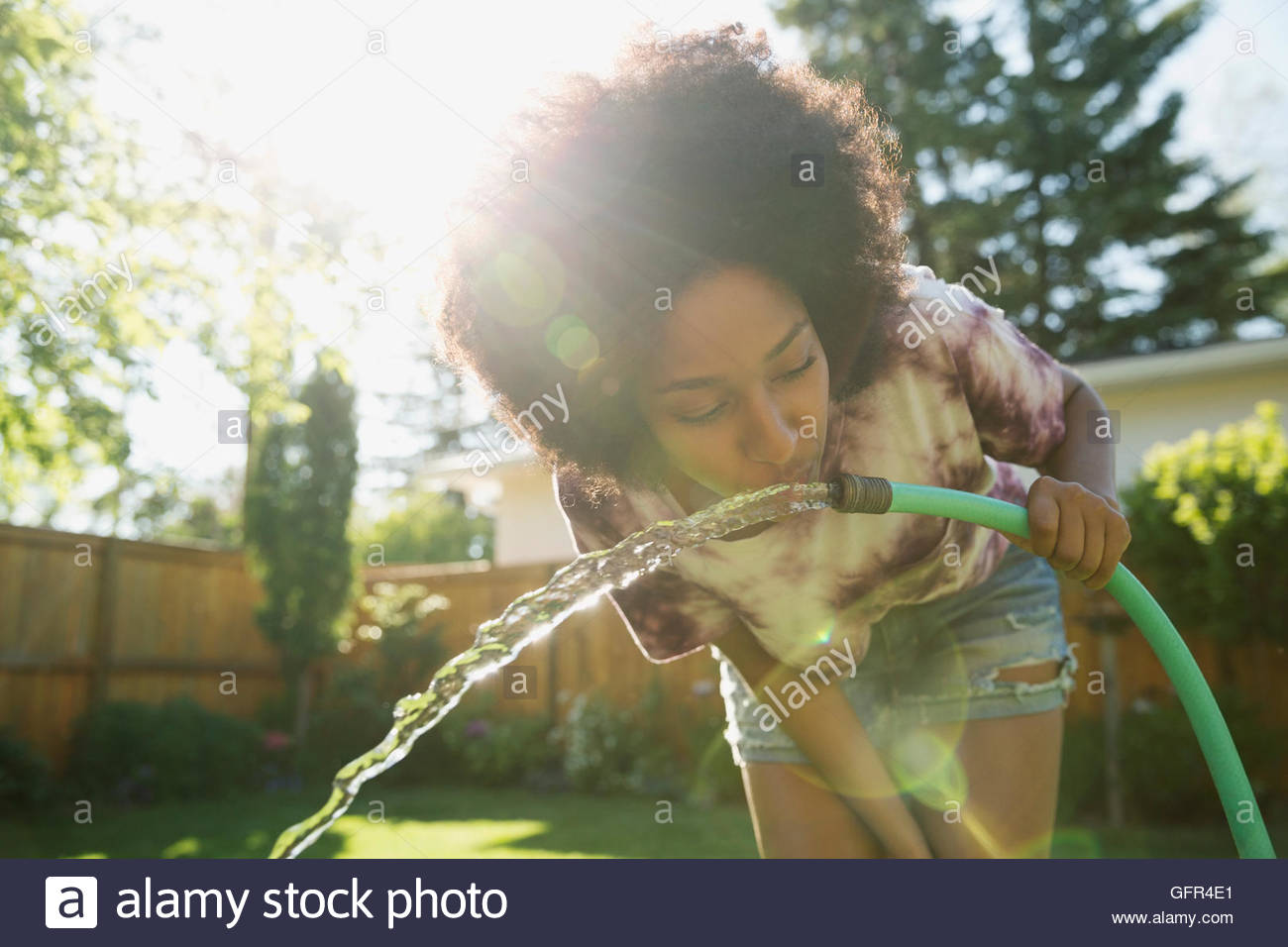 Woman drinking water from hose in sunny backyard Stock Photo Alamy