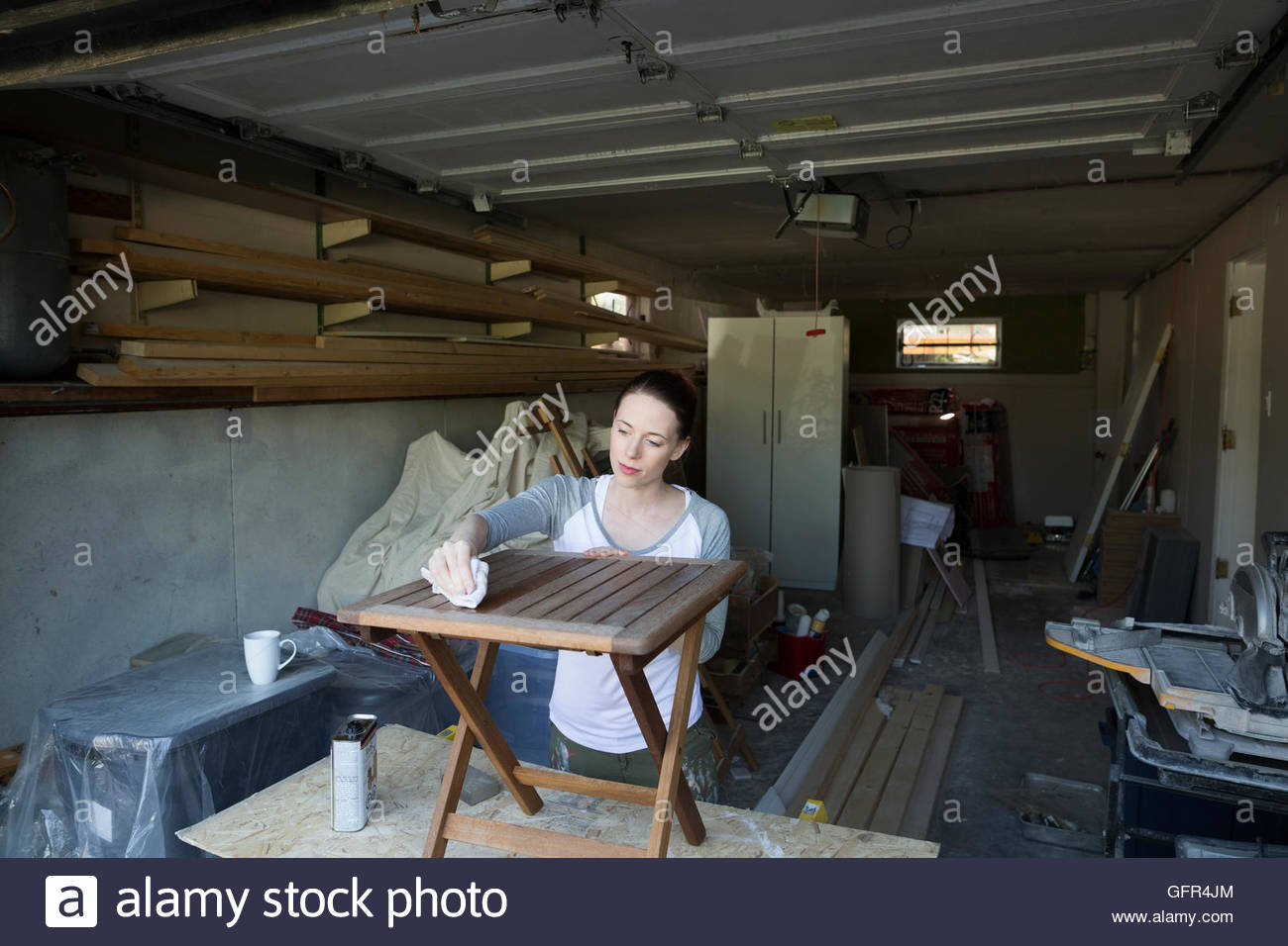 Woman staining wood furniture home improvement project in garage Stock