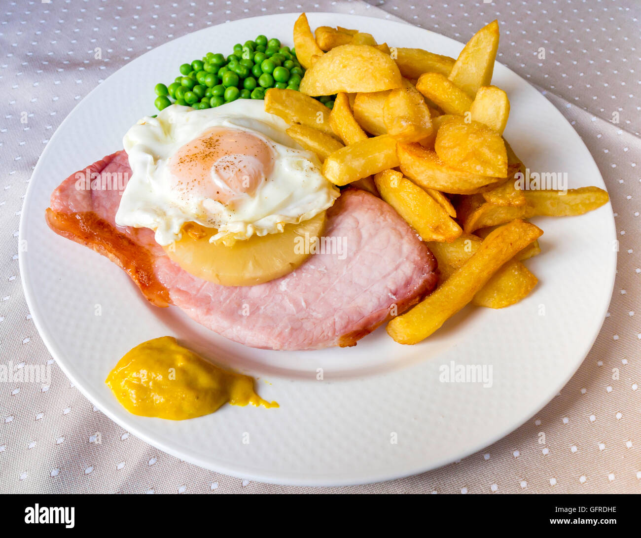 Meal of gammon rasher fried egg potato chips pineapple peas and Stock