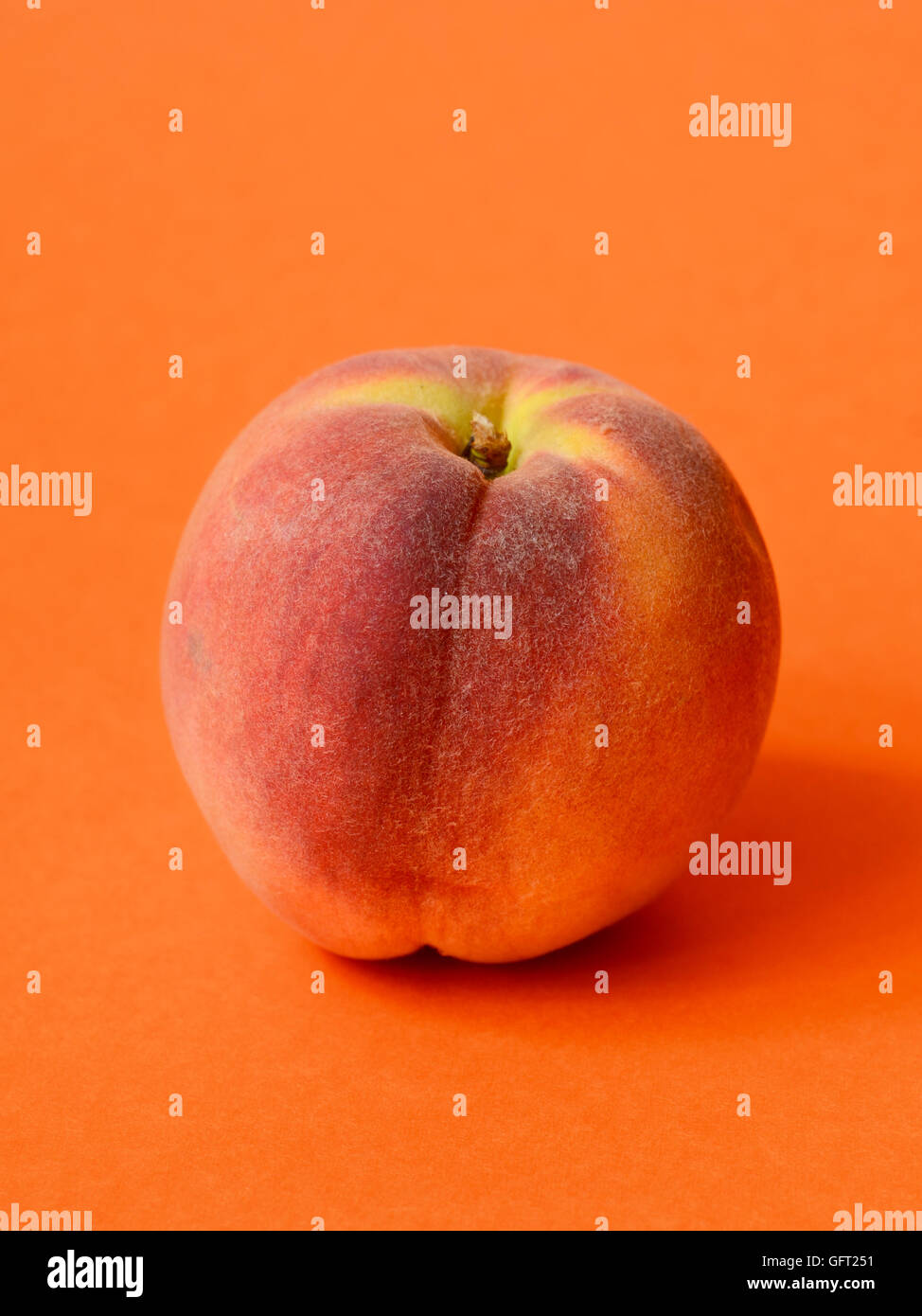 One ripe peach on orange colored background Stock Photo