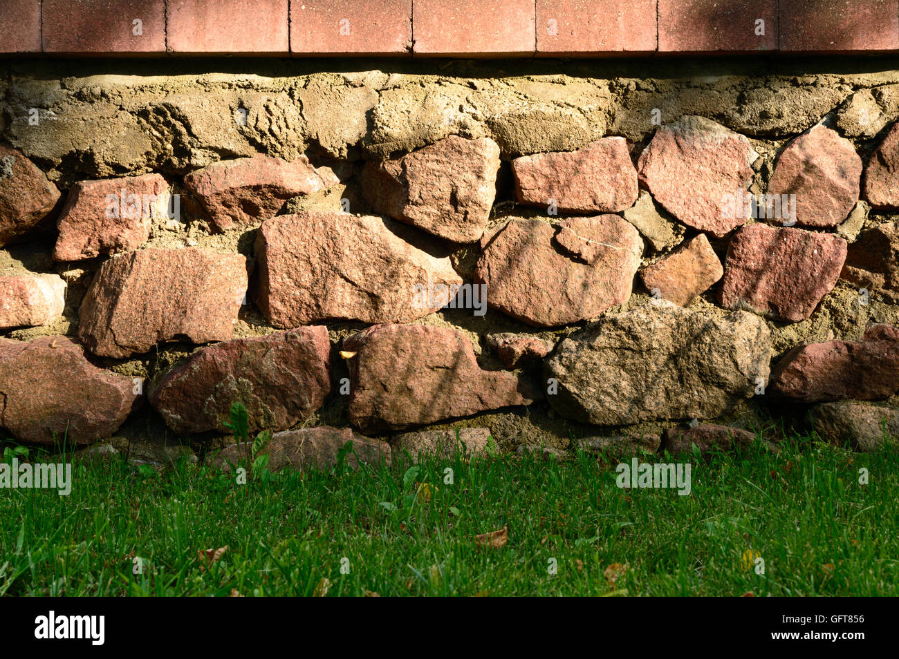 Brick and stone wall closeup with green weed below Stock Photo - Alamy