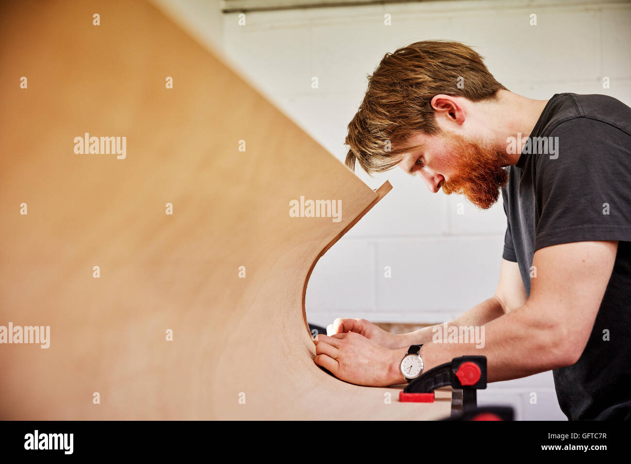 A  man using a tool on the curved cut out edge of a piece of wood Stock Photo