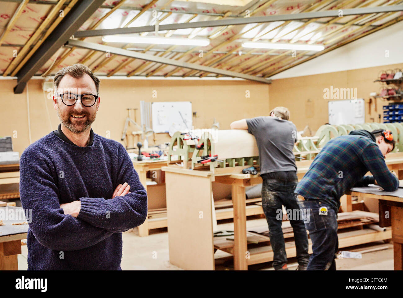 A furniture ,Two people working and a man standing with arms