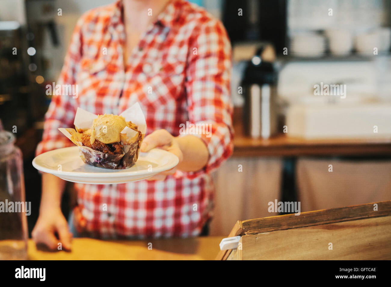 A woman in a coffee shop holding out a plate with a fresh muffin with a scoop of ice cream Stock Photo