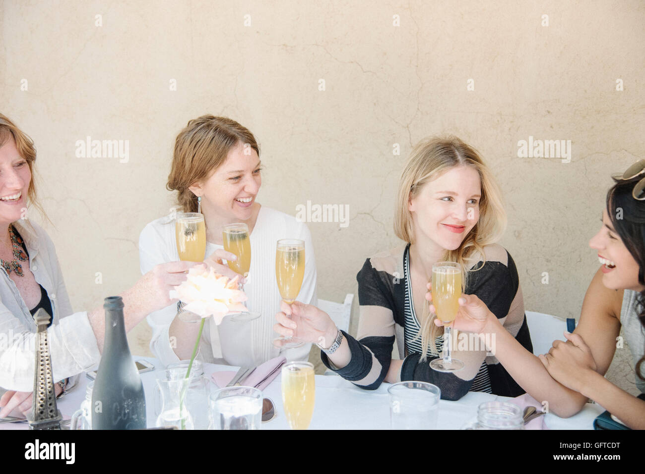 Four smiling women sitting at a table holding glasses of champagne toasting Stock Photo