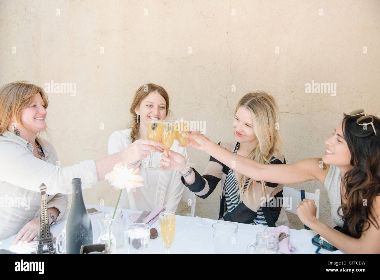 Four smiling women sitting at a table holding glasses of champagne toasting Stock Photo