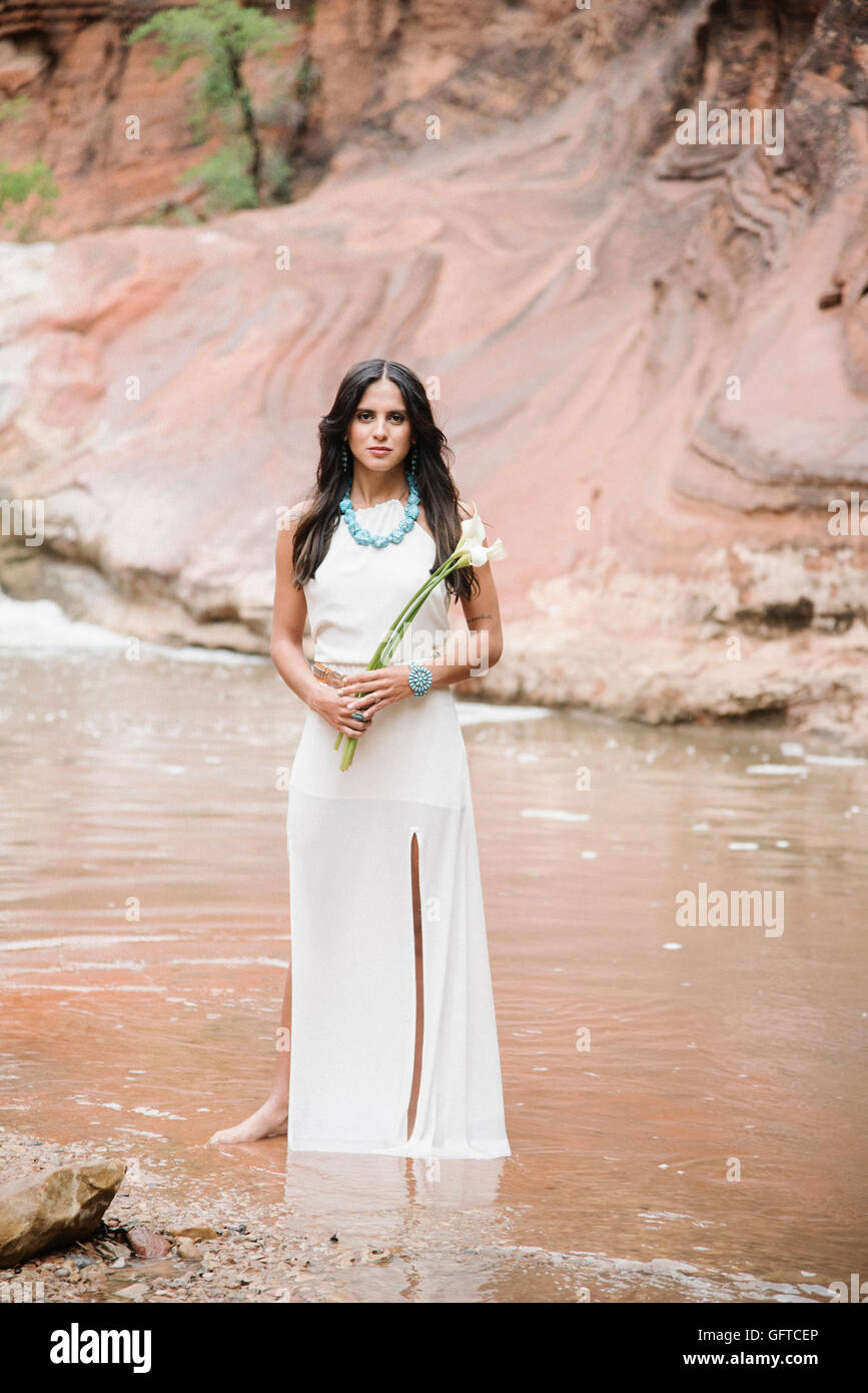 Young woman with long brown hair wearing a long white dress standing by ...