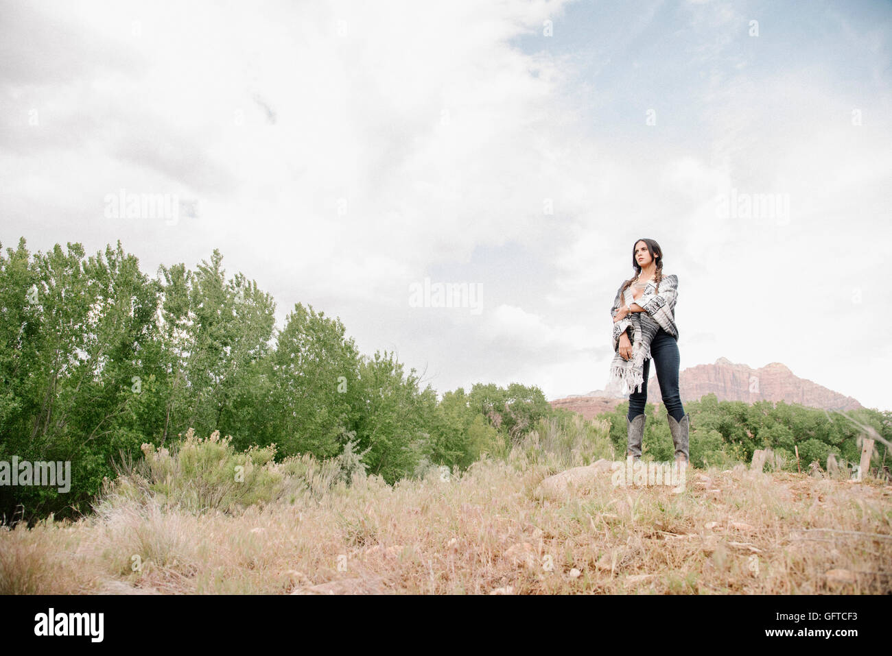 Young woman with long brown hair standing in a prairie under a cloudy sky Stock Photo