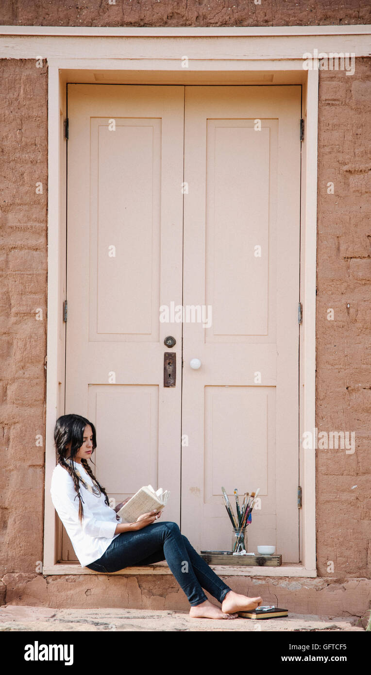 Young woman with long brown hair sitting on the ground outside the front door of a building Stock Photo