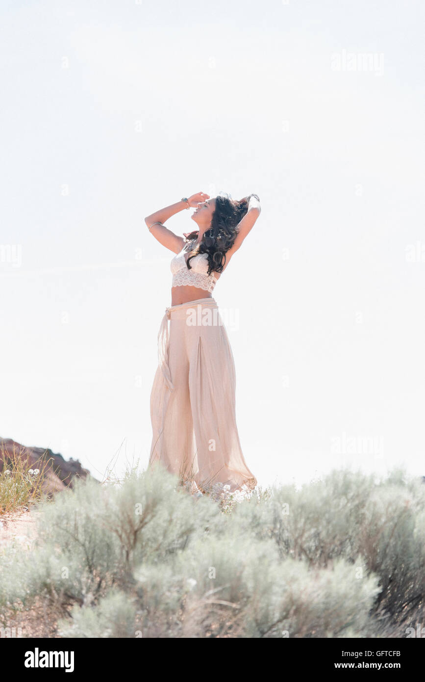 Young woman with long brown hair wearing a long white dress standing in the prairie Stock Photo