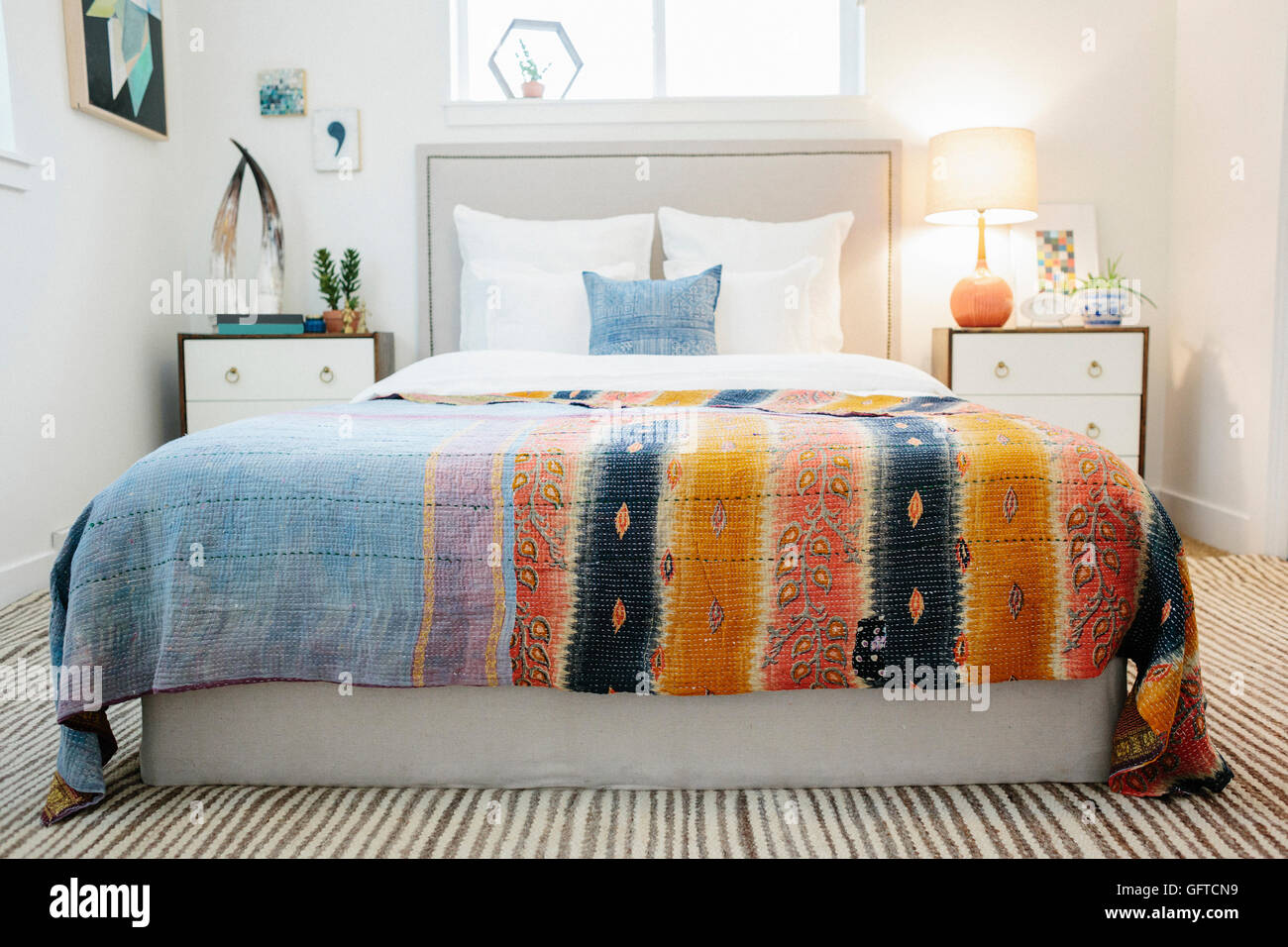A bedroom in an apartment with a double bed and beside cabinets and a vivid striped patterned bedspread Stock Photo