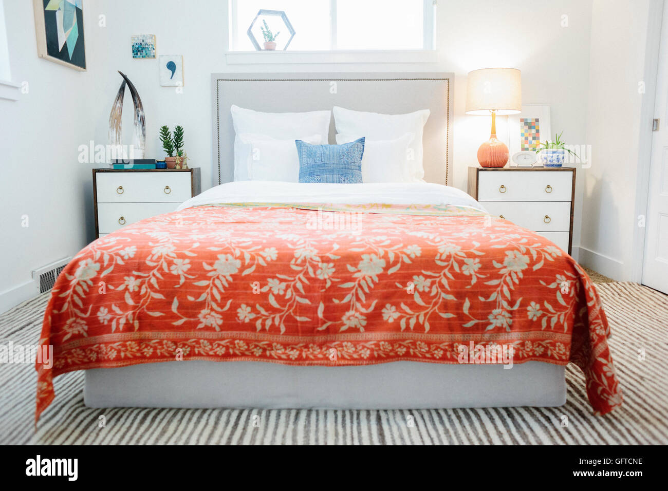 A bedroom in an apartment with a double bed and beside cabinets and a vivid russet coloured bedspread with a floral pattern Stock Photo