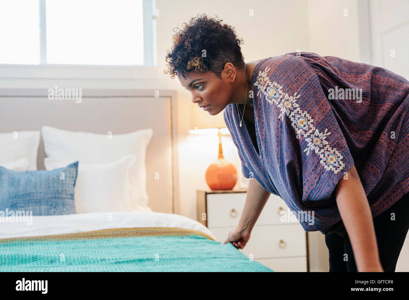A woman smoothing a throw over a double bed in a bedroom. Stock Photo