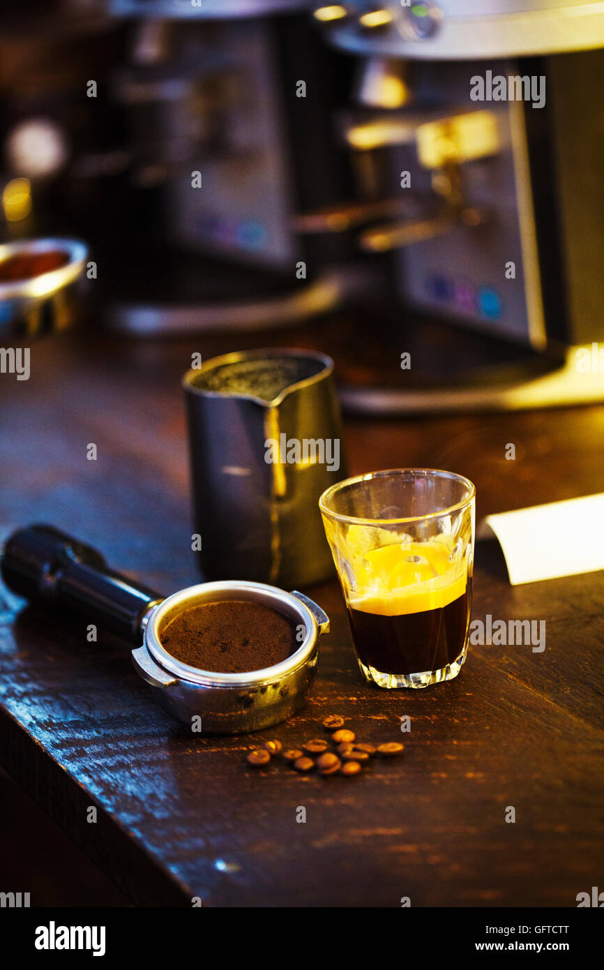 A coffee machine grounds holder a heap of coffee beans and a glass cup
