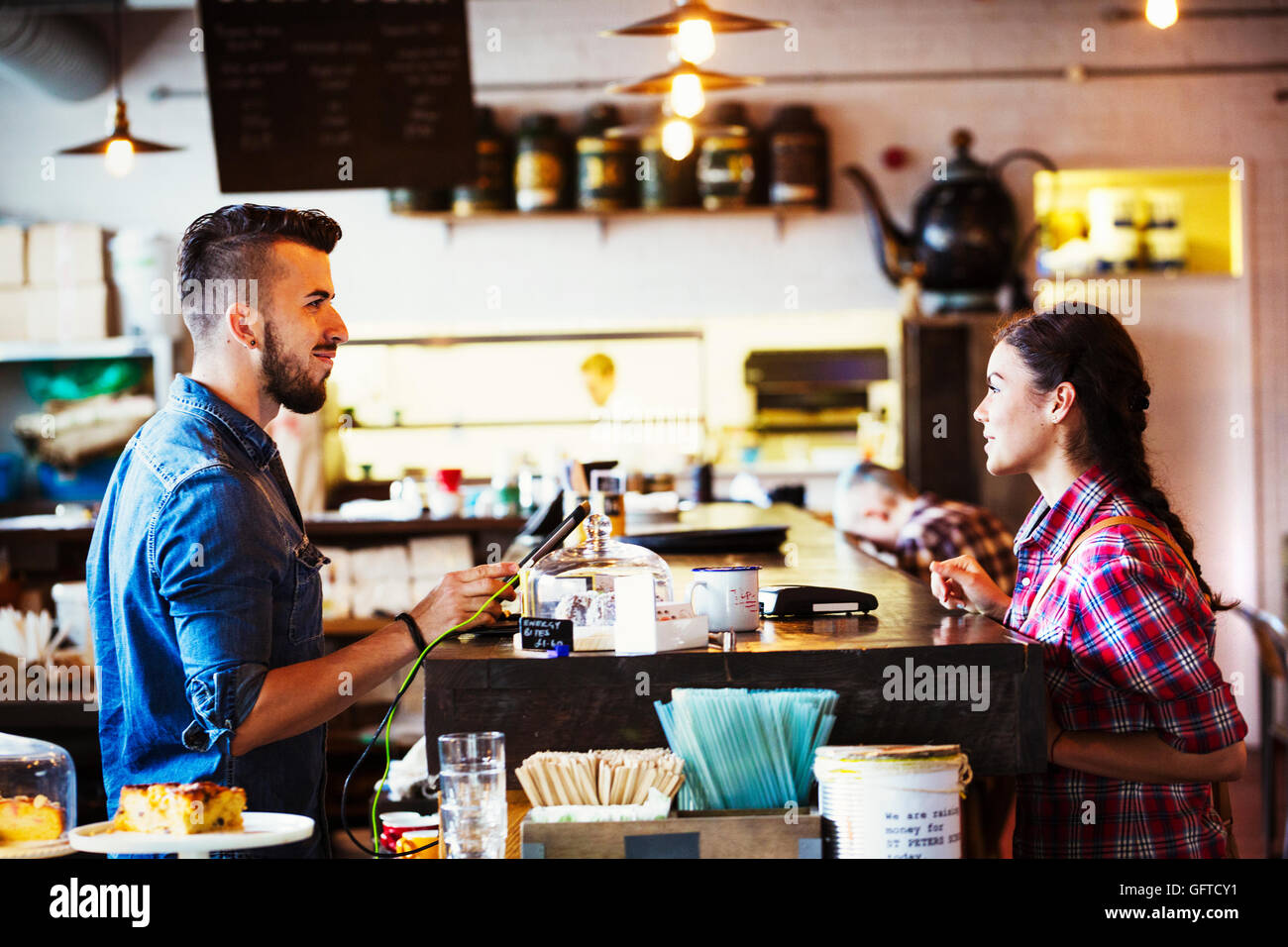 A man behind the counter using a touch screen to record transactions and a woman customer Stock Photo