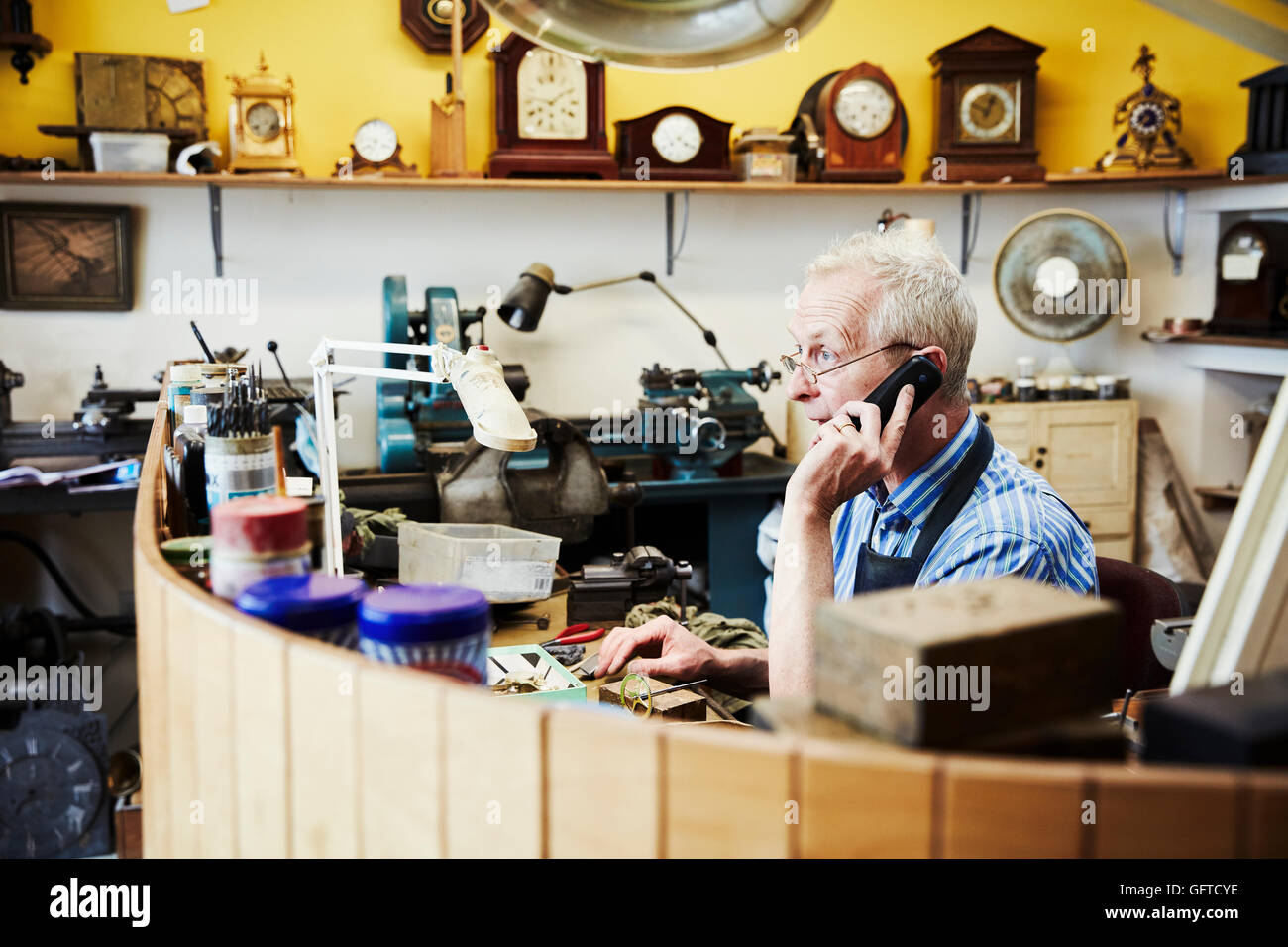 A clock maker on the phone in his workshop Stock Photo