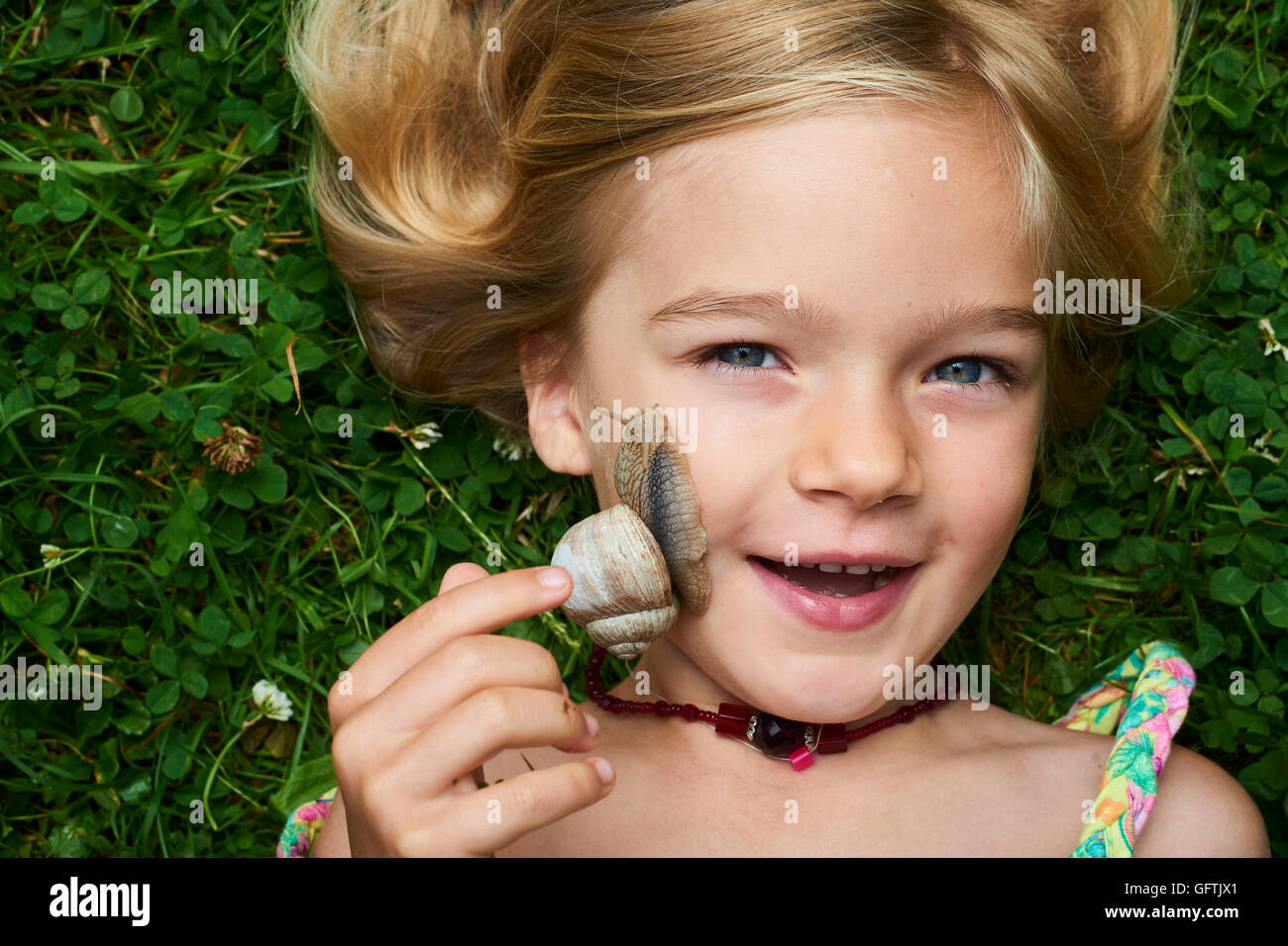 Closeup portrait of cute blond child girl with snail on her face. Terrified facial expression Stock Photo