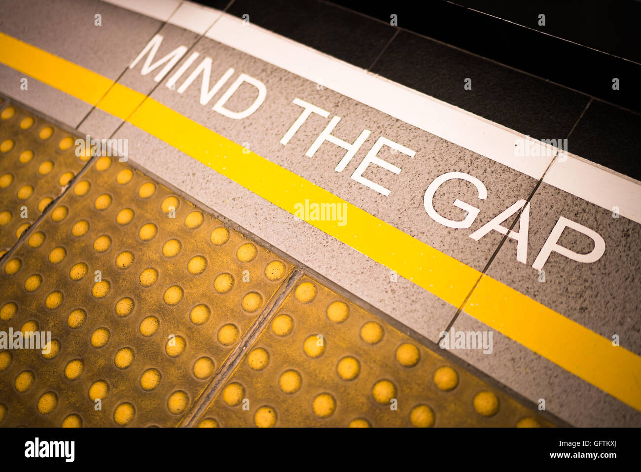 Mind the gap sign painted on train station's platform edge, conceptual, vignette darken edge, depth of field blur on far end Stock Photo