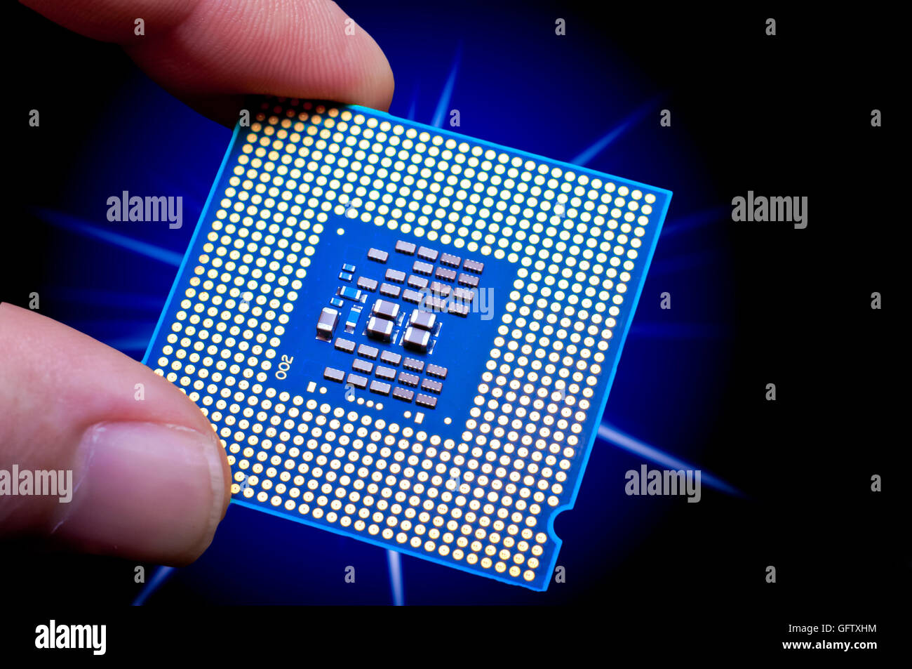 Glowing blue computer CPU held between finger and thumb in front of starburst on a black backgound Stock Photo