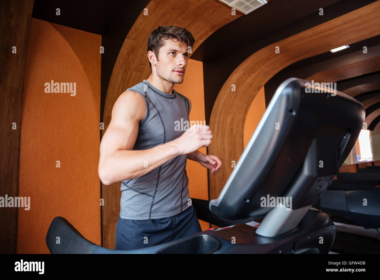 Young handsome sports man in sportswear running on treadmill at gym