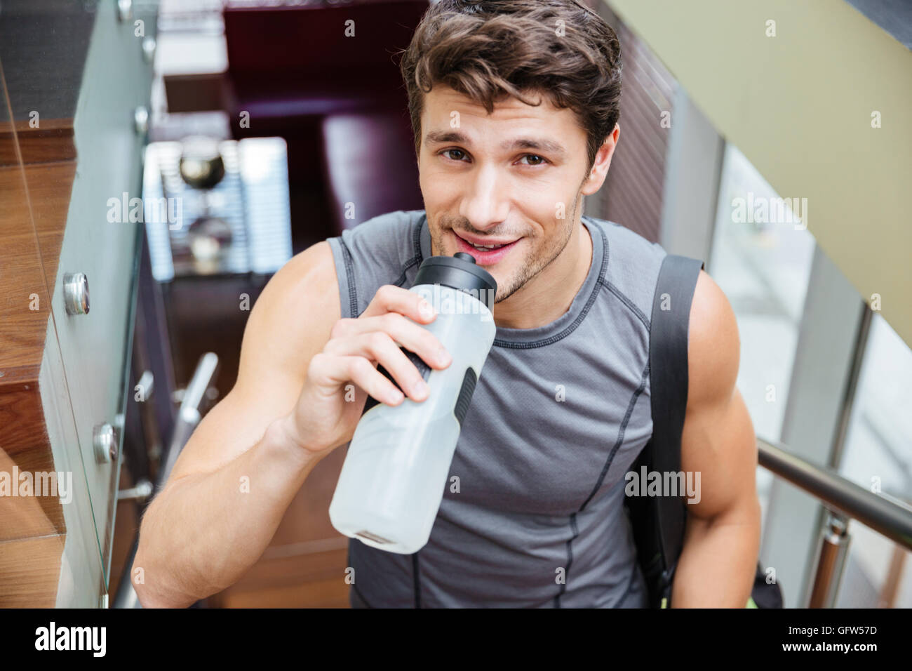 Smiling handsome young man athlete walking and drinking water after