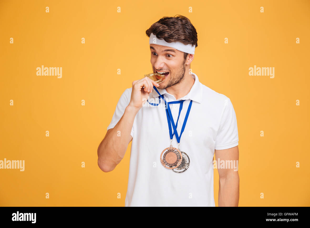 Closeup of handsome young man athlete biting his medal over yellow background Stock Photo