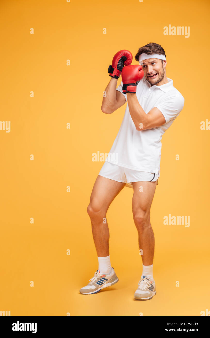 Scared young man boxer in red gloves covered face by hands over yellow background Stock Photo