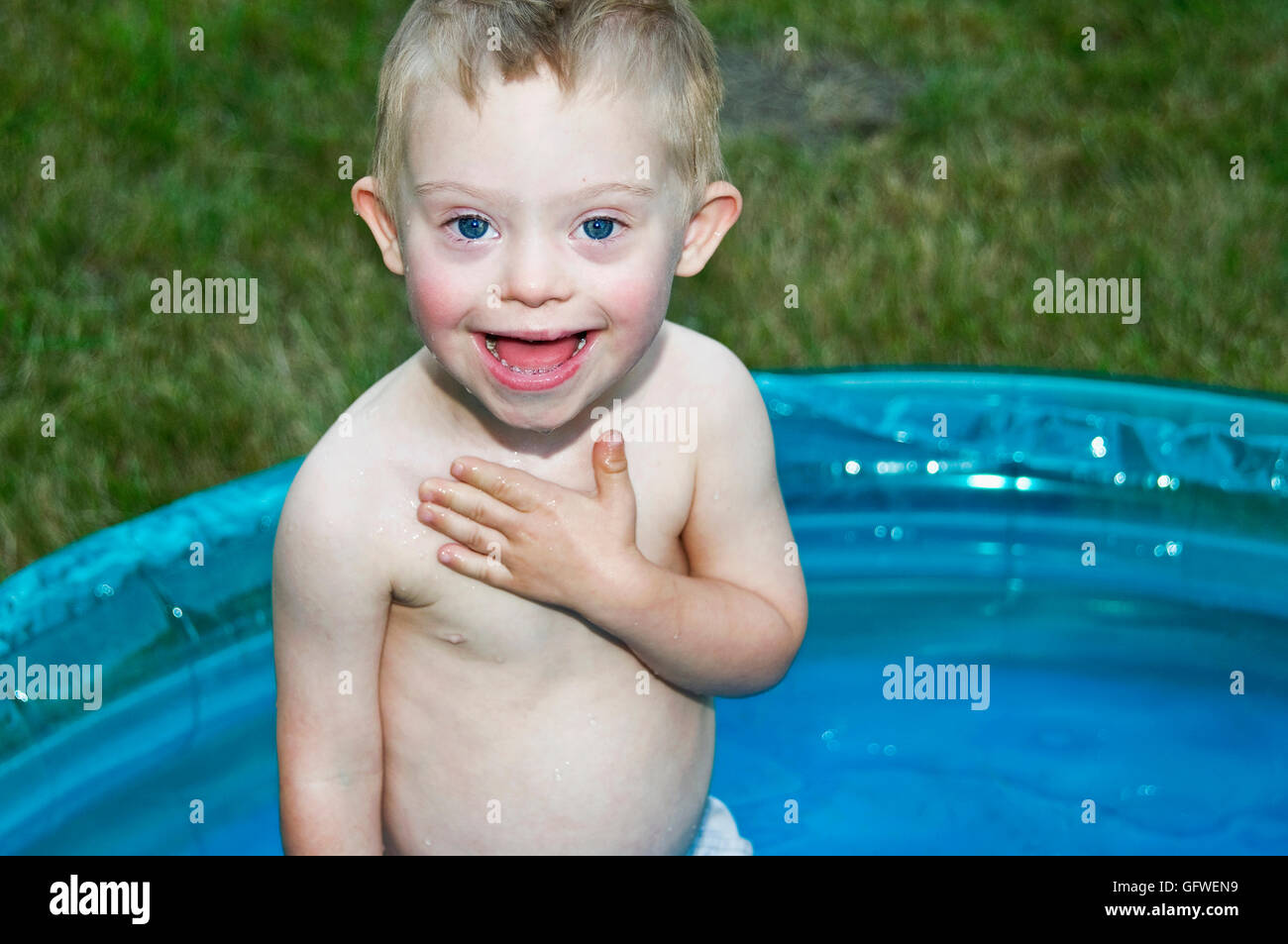 A young boy with downs syndrome playing in a kiddie pool and making a sign language gesture. Stock Photo