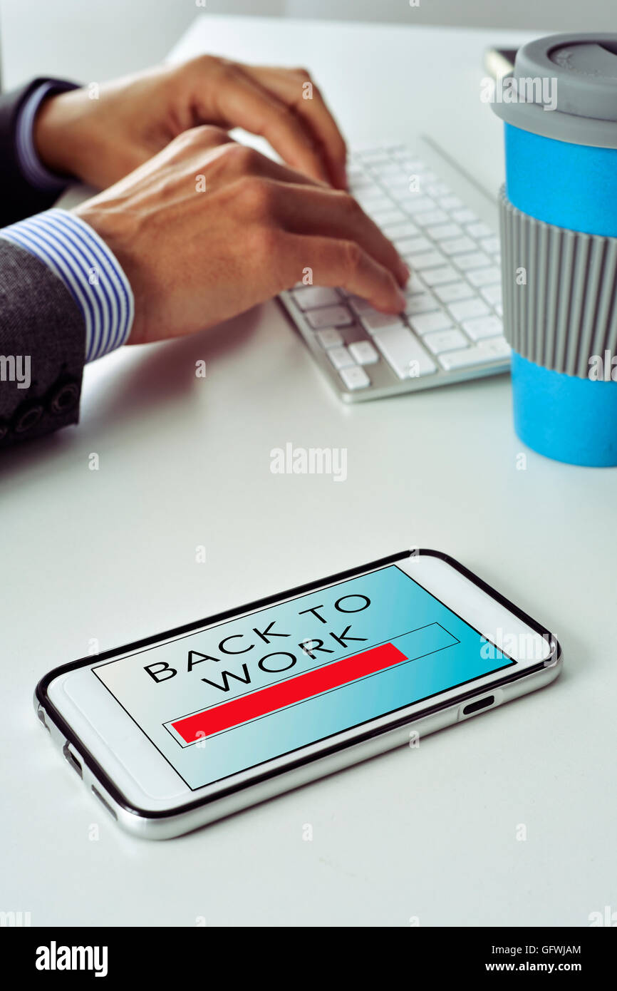 closeup of a smartphone with the text back to work in its screen, on the office desk of a businessman who is typing in the keybo Stock Photo