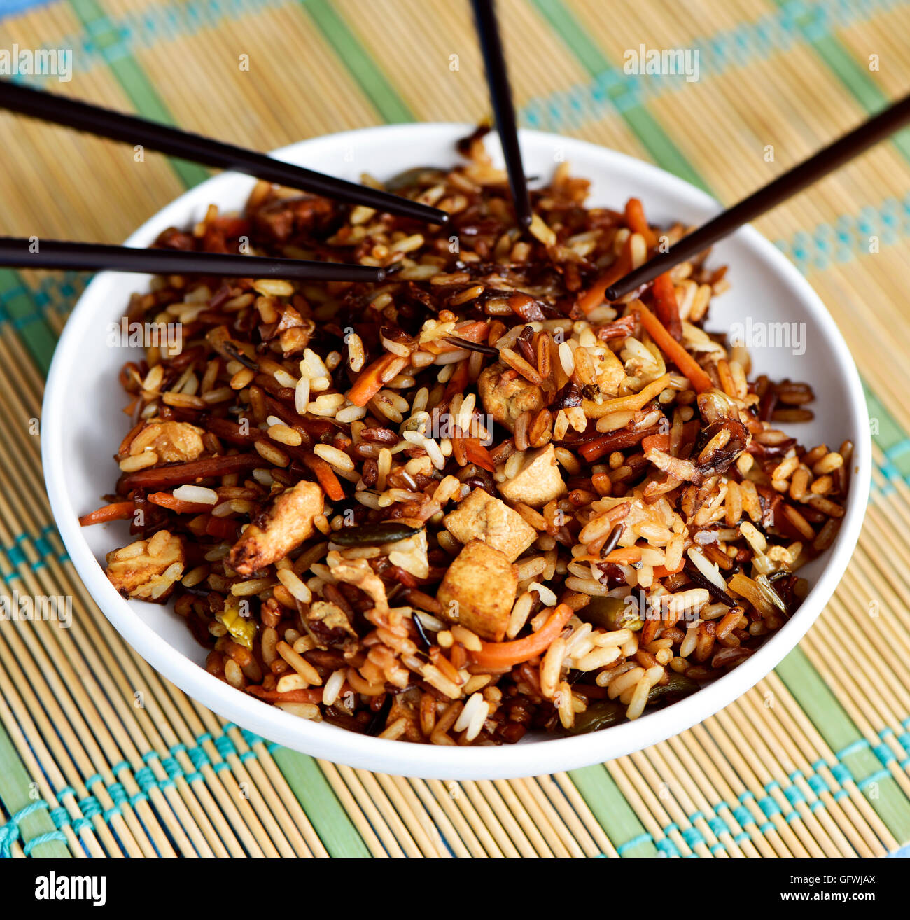 closeup of a white ceramic bowl with appetizing asian fried rice and some chopsticks, on a bamboo mat Stock Photo