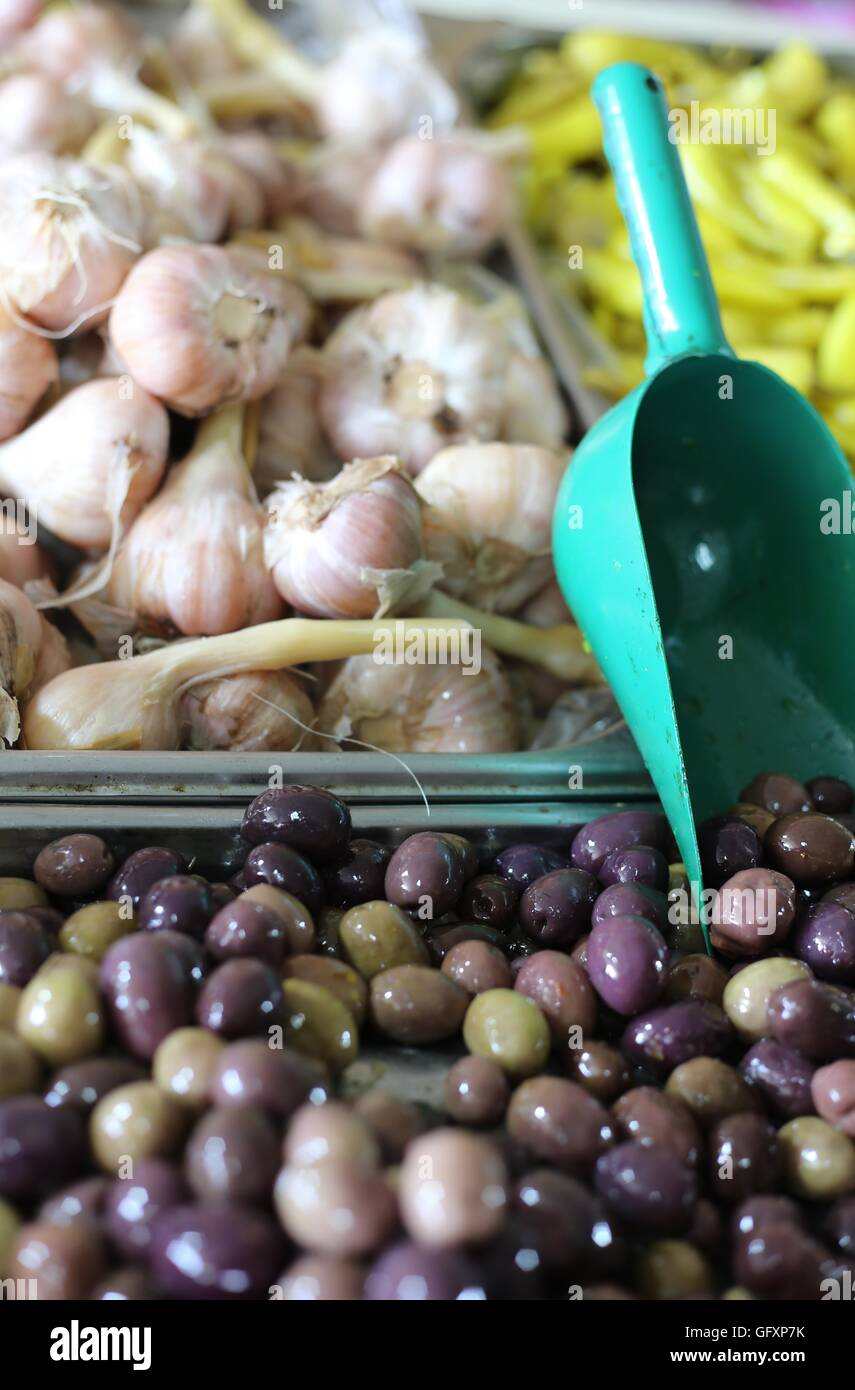 Olives and Garlic. Spicy black olives, pickled garlic heads and green chilli pepper with sauce in a market stand. Close up of appetizers and pickles Stock Photo