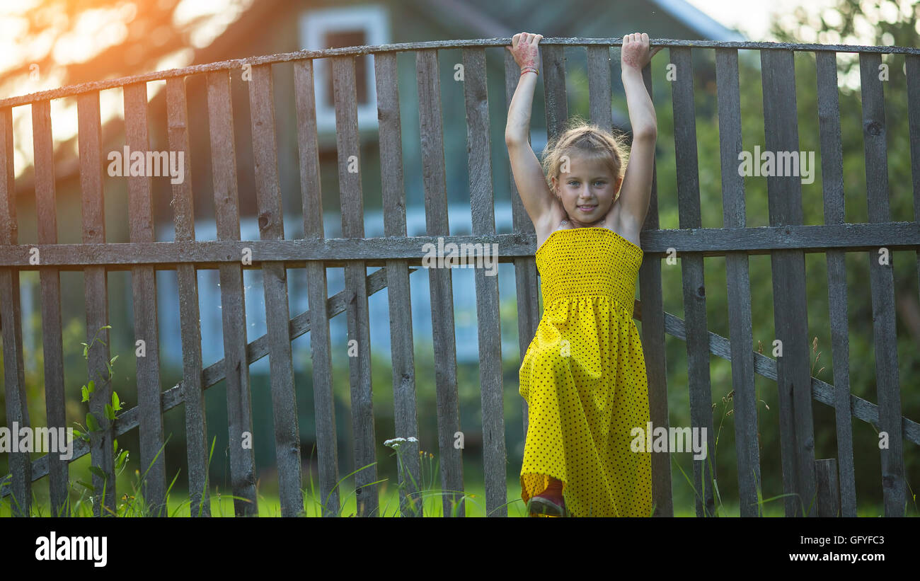 Little girl near the wood fence of a village house. Stock Photo