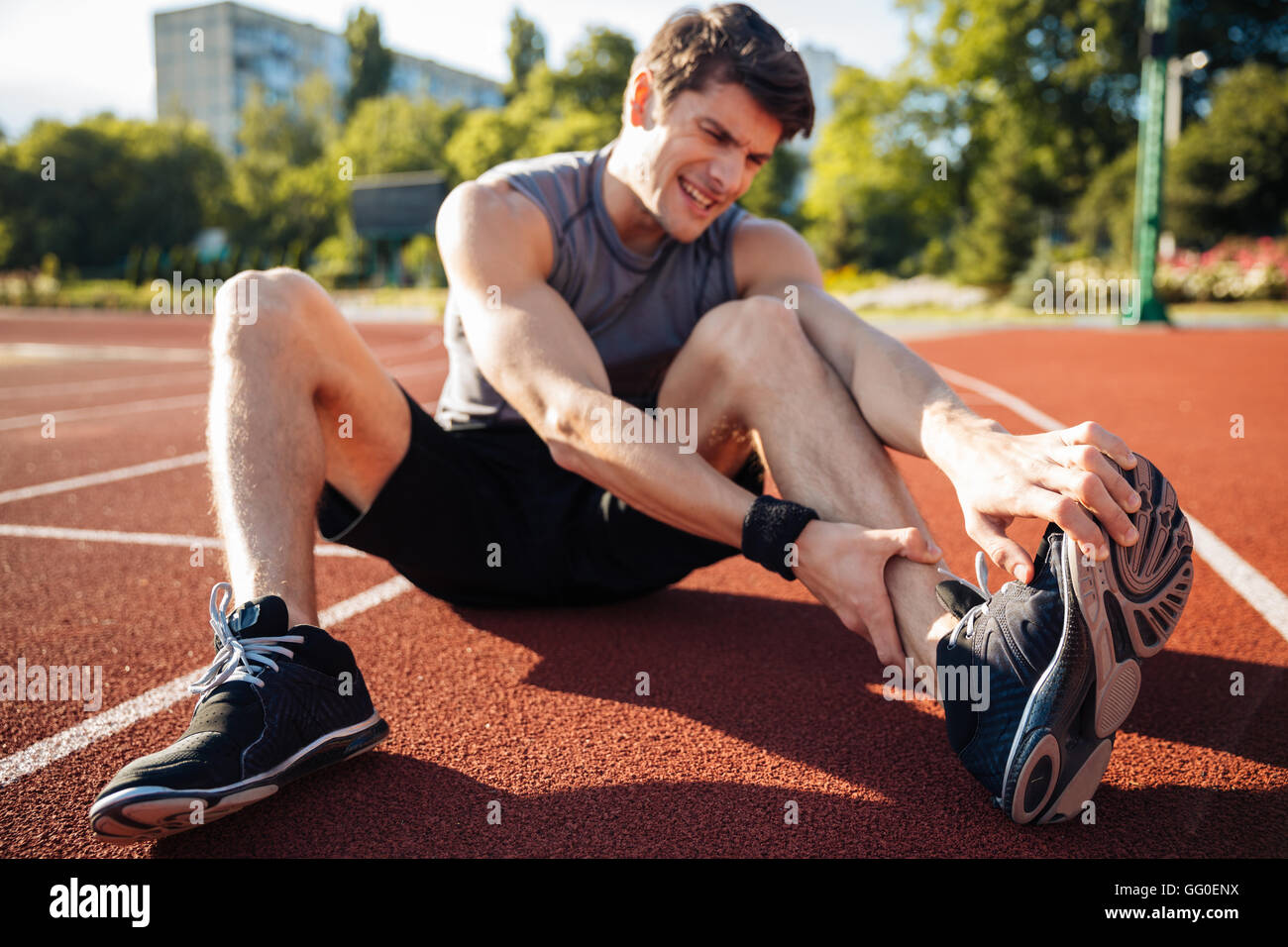 Young male runner suffering from leg cramp on the track at the stadium