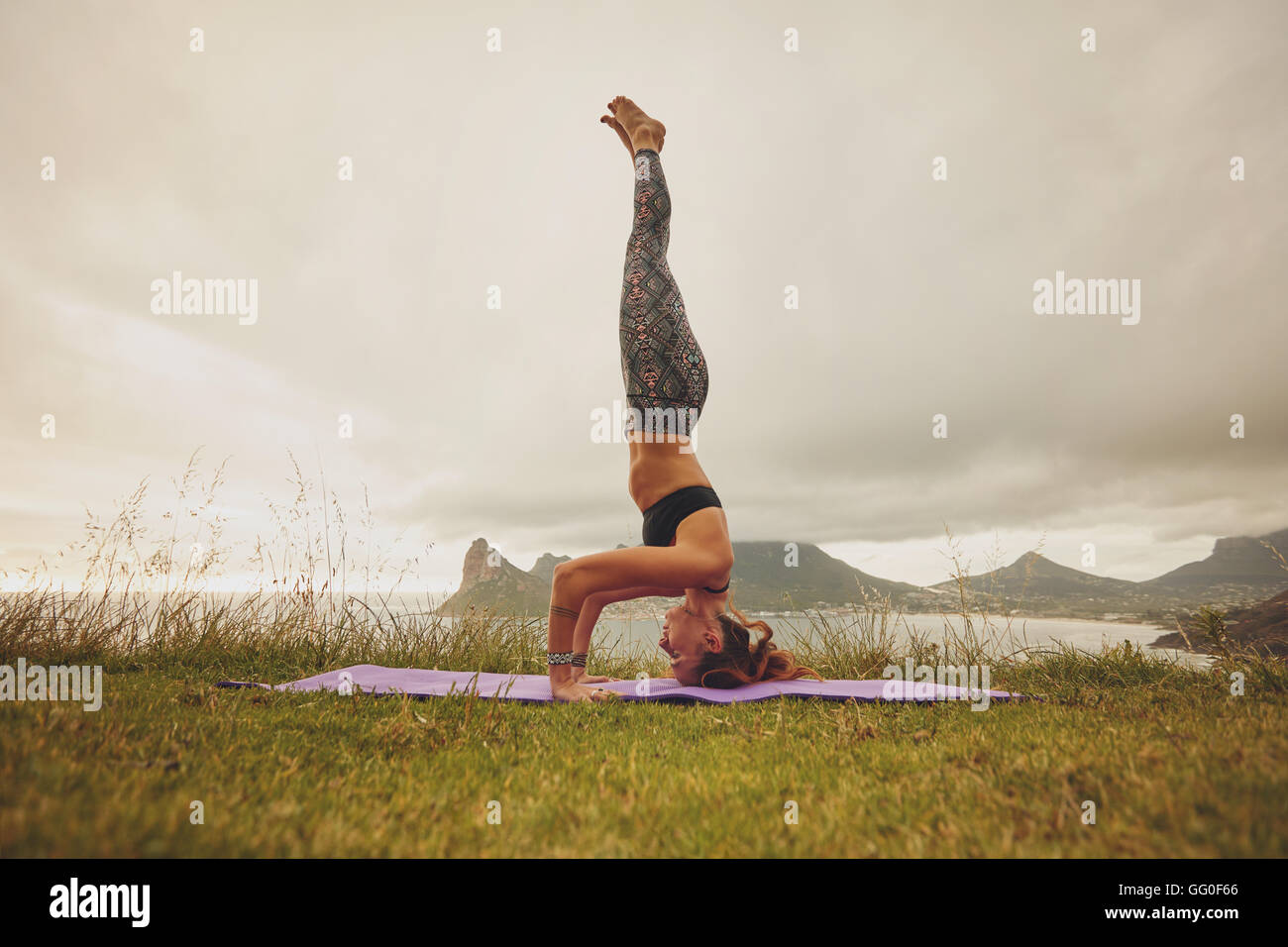 Full length shot of young woman practicing sirsasana yoga. fitness woman doing the headstand yoga outdoors on meadow. Stock Photo