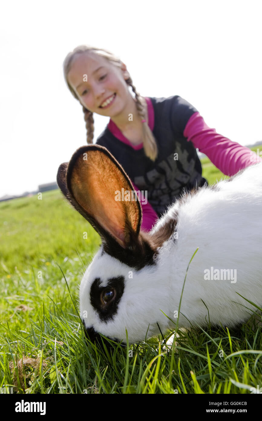 Pet rabbit eating grass and young girl 10 years age caring happy Stock