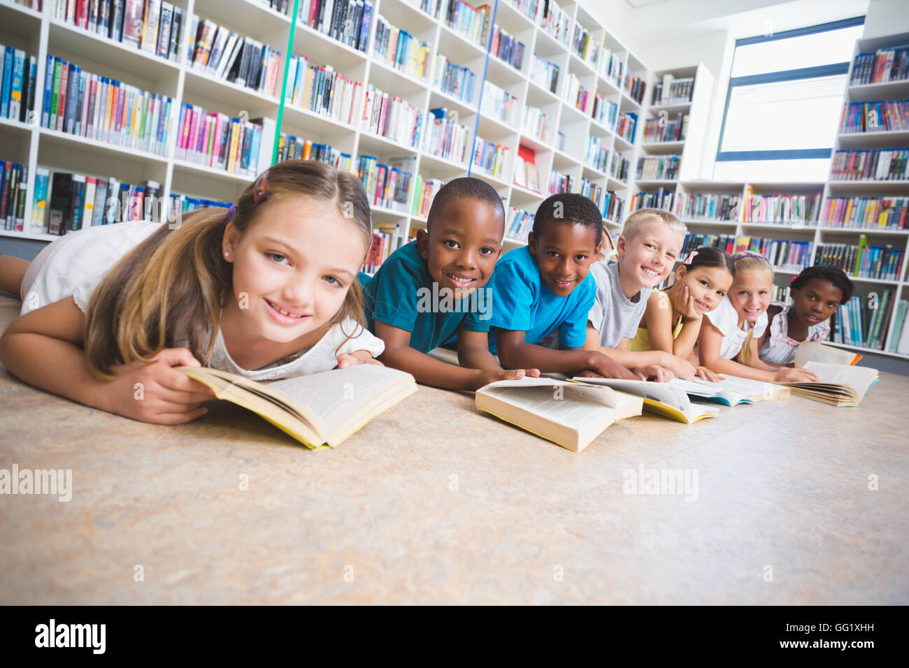 Smiling school kids lying on floor reading book in library Stock Photo ...