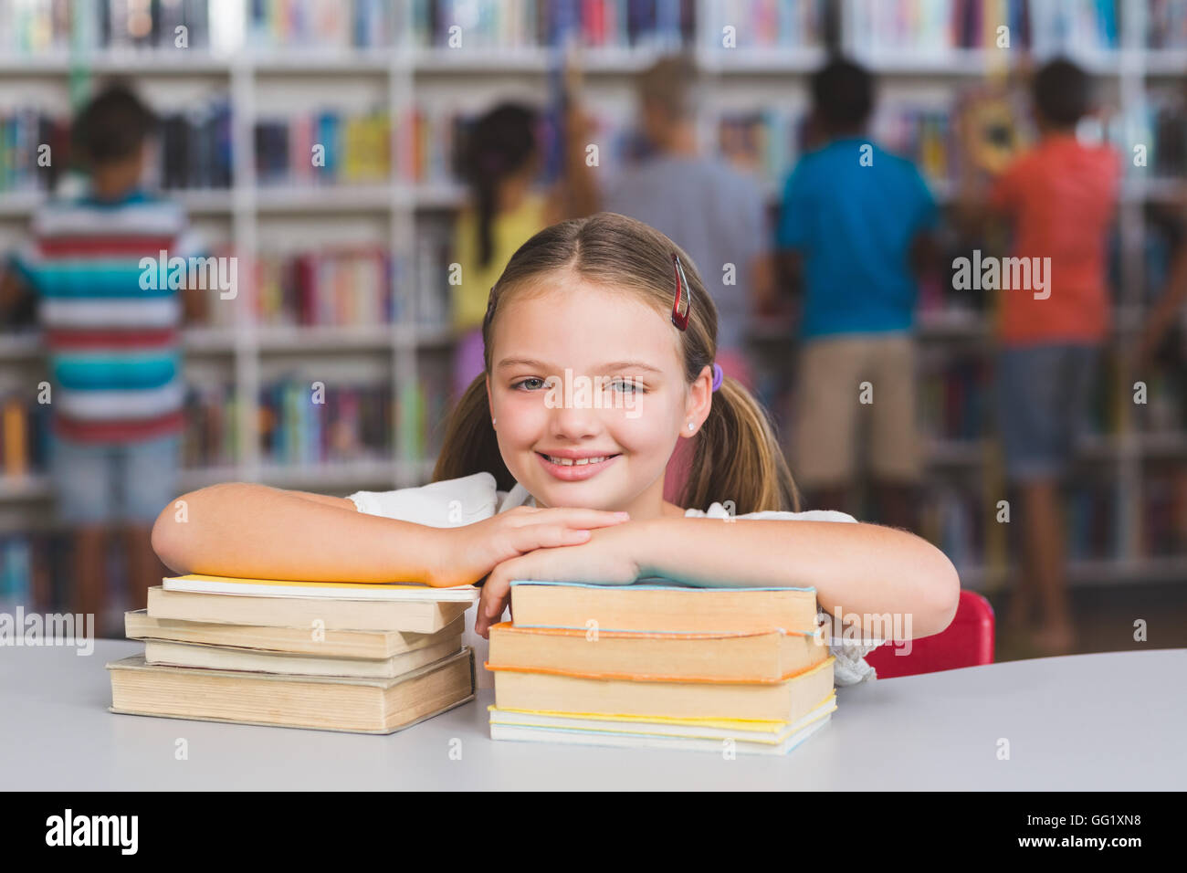 Smiling girl leaning on pile of books in library Stock Photo - Alamy