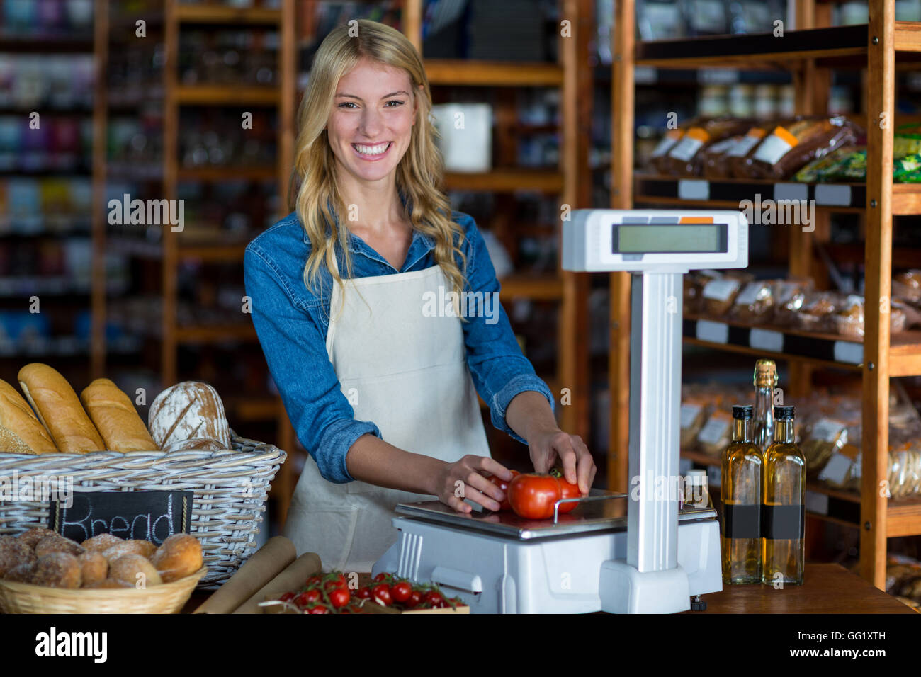 Smiling female staff weighting vegetables on scale in supermarket Stock Photo