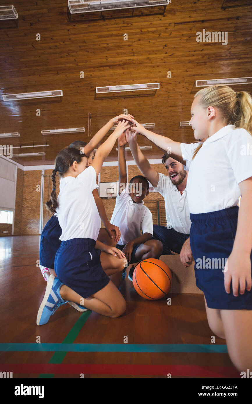 Sports teacher and school kids forming hand stack in basketball court