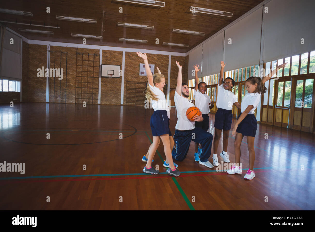 Sports teacher and school kids playing in basketball court Stock Photo