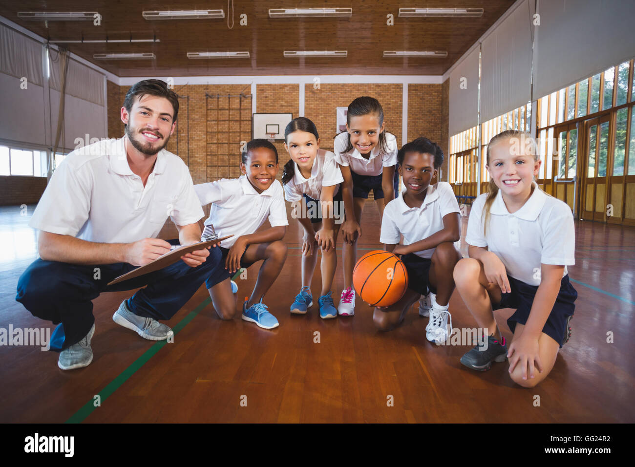 Portrait of sports teacher and school kids in basketball court Stock Photo