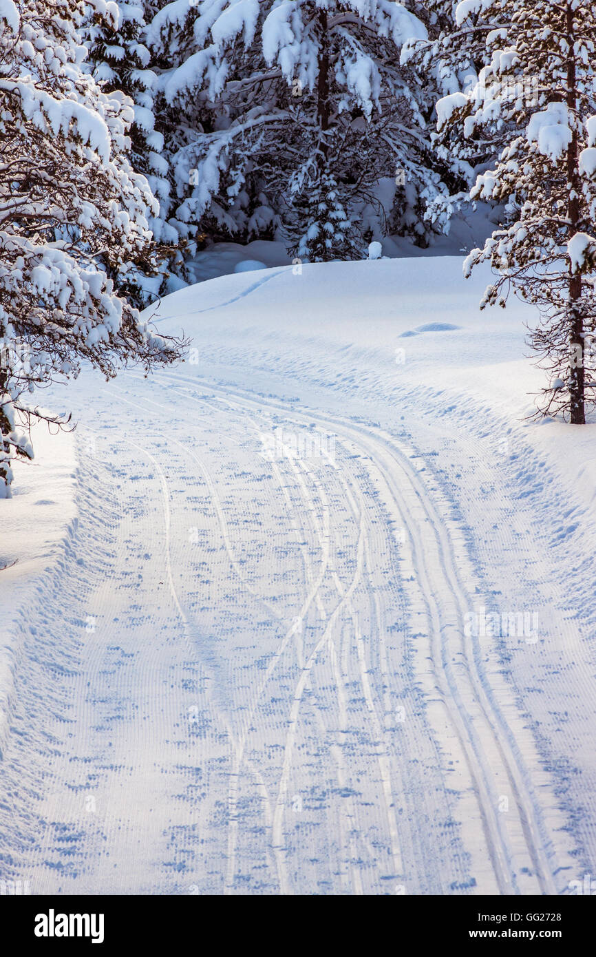 One machine made track on the right, and tracks from skiers on the flat part of the road on the left, visible in the snow. Stock Photo