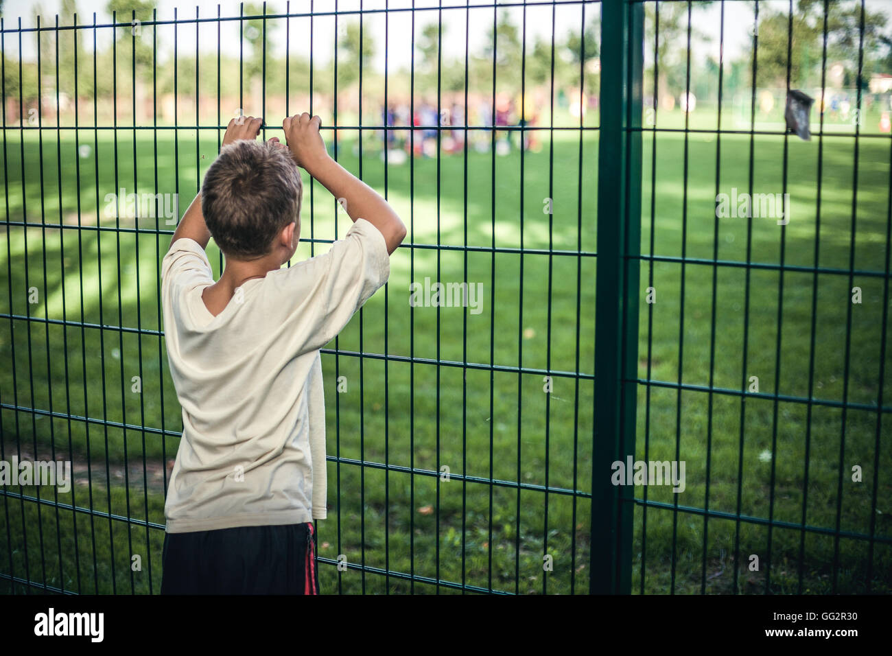 a-young-lonely-boy-11-watching-a-game-through-fence-GG2R30.jpg