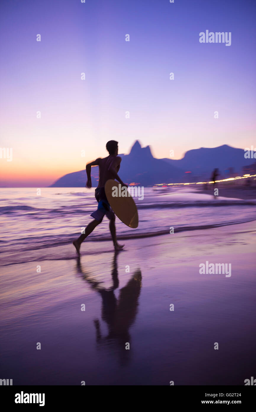 Sunset silhouette of carioca Brazilian running with skimboard on Ipanema Beach Rio de Janeiro, Brazil Stock Photo