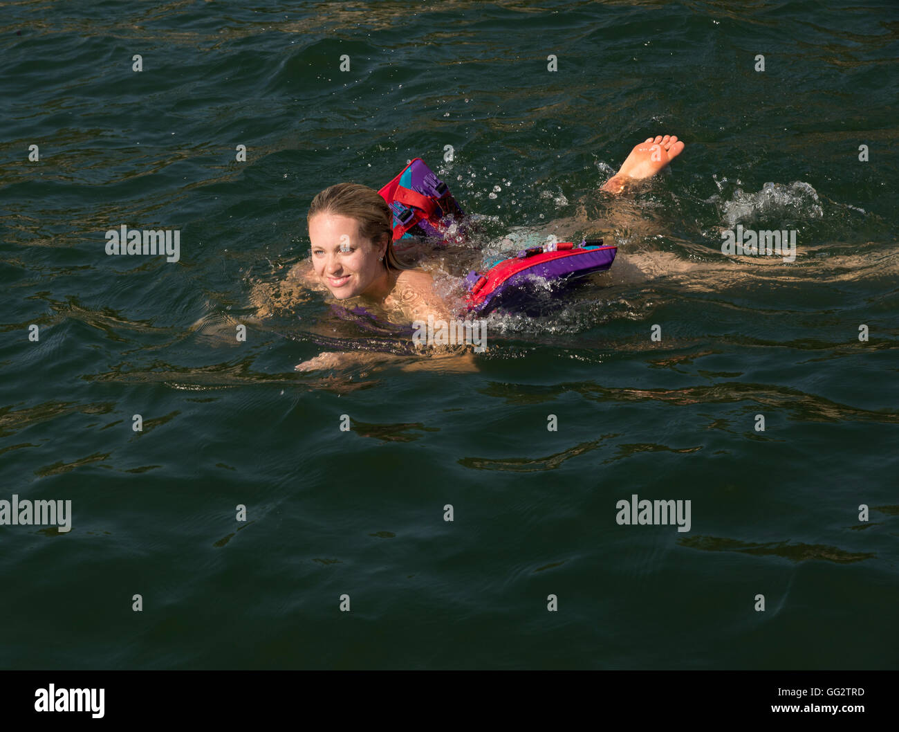 A fun-loving 20's woman swims in a lake. Stock Photo