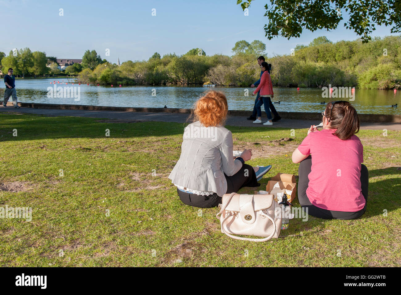 Two young women having a chip supper/picnic at The Lough, Cork, Ireland on a gorgeous summers evening. Stock Photo